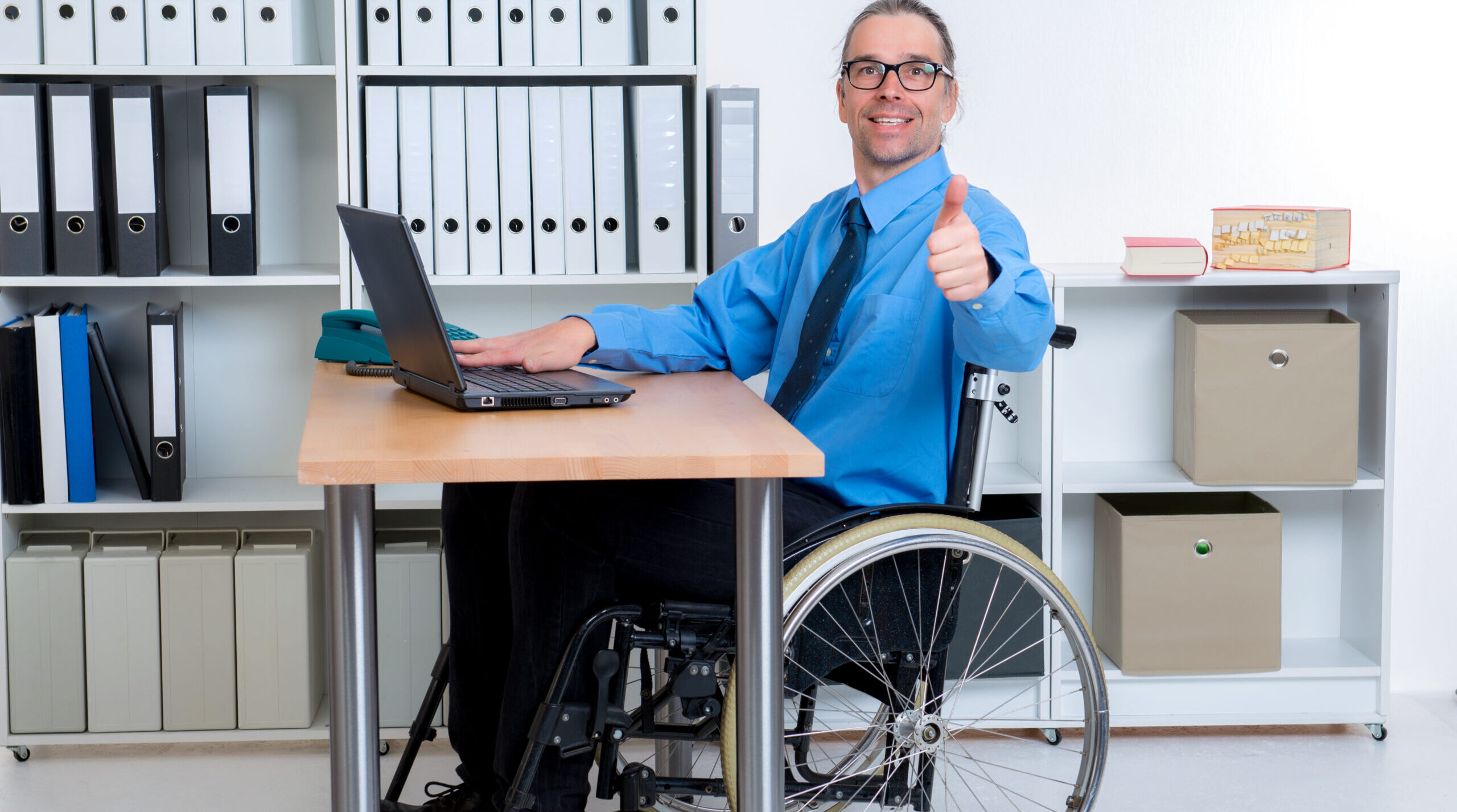 A business man in a wheelchair sitting at a desk.